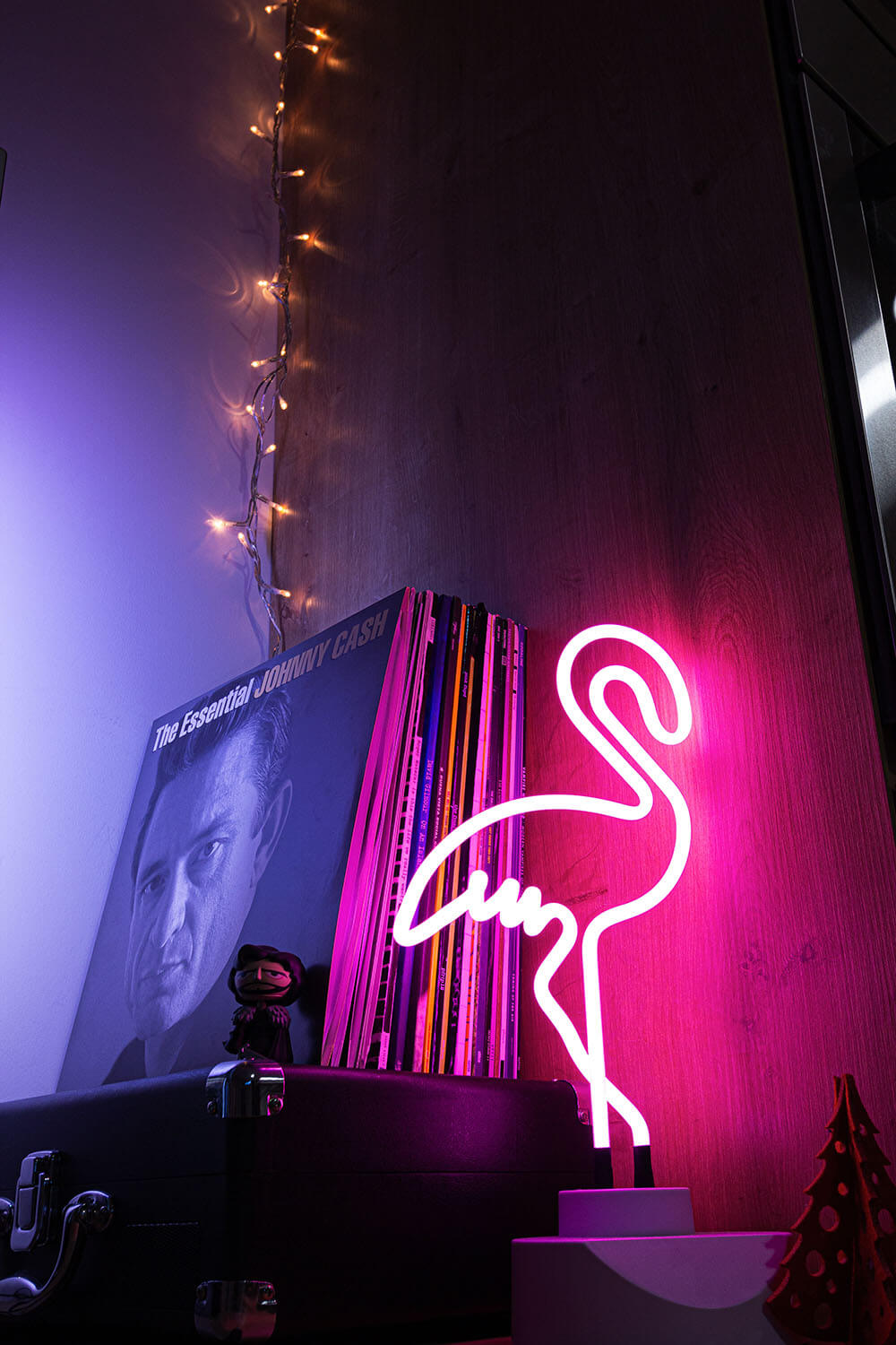 En Flamingo i neonlampe fra Posters lyser på en hylde ved siden af en Johnny Cash-vinyl, en vintageplakat, lyskæder ovenover og flere plader stablet bagved.