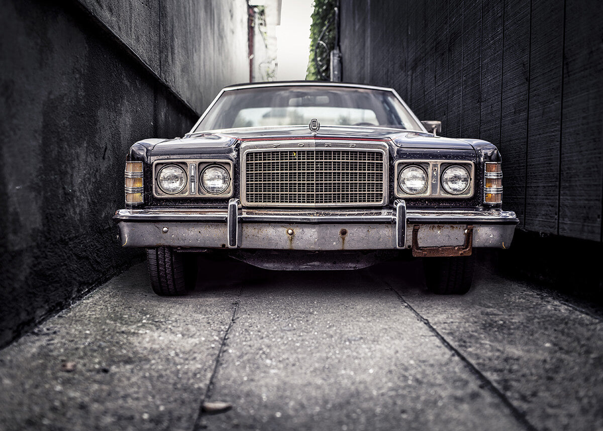 En Ford LTD by Posters er parkeret i en smal gyde, og forfra kan man se en stor kromgrill og rektangulære forlygter - tidløs retrostil og klassisk elegance, som taget direkte ud af en veteranbilplakat.