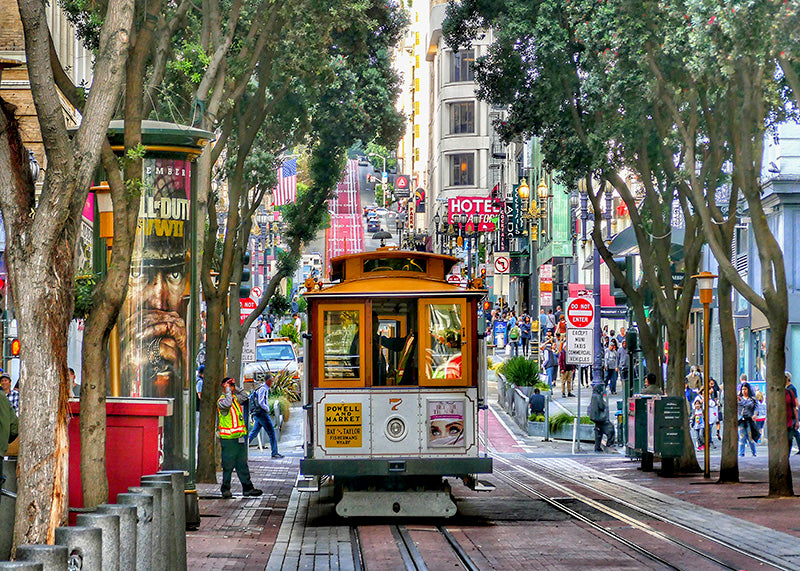 Plakaten "Historisk sporvogn på Powell Street" fanger en klassisk San Francisco sporvogn på Powell Street omgitt af trær, butikker og folk-perfekt for dig som ønsker et livlig bymotiv.