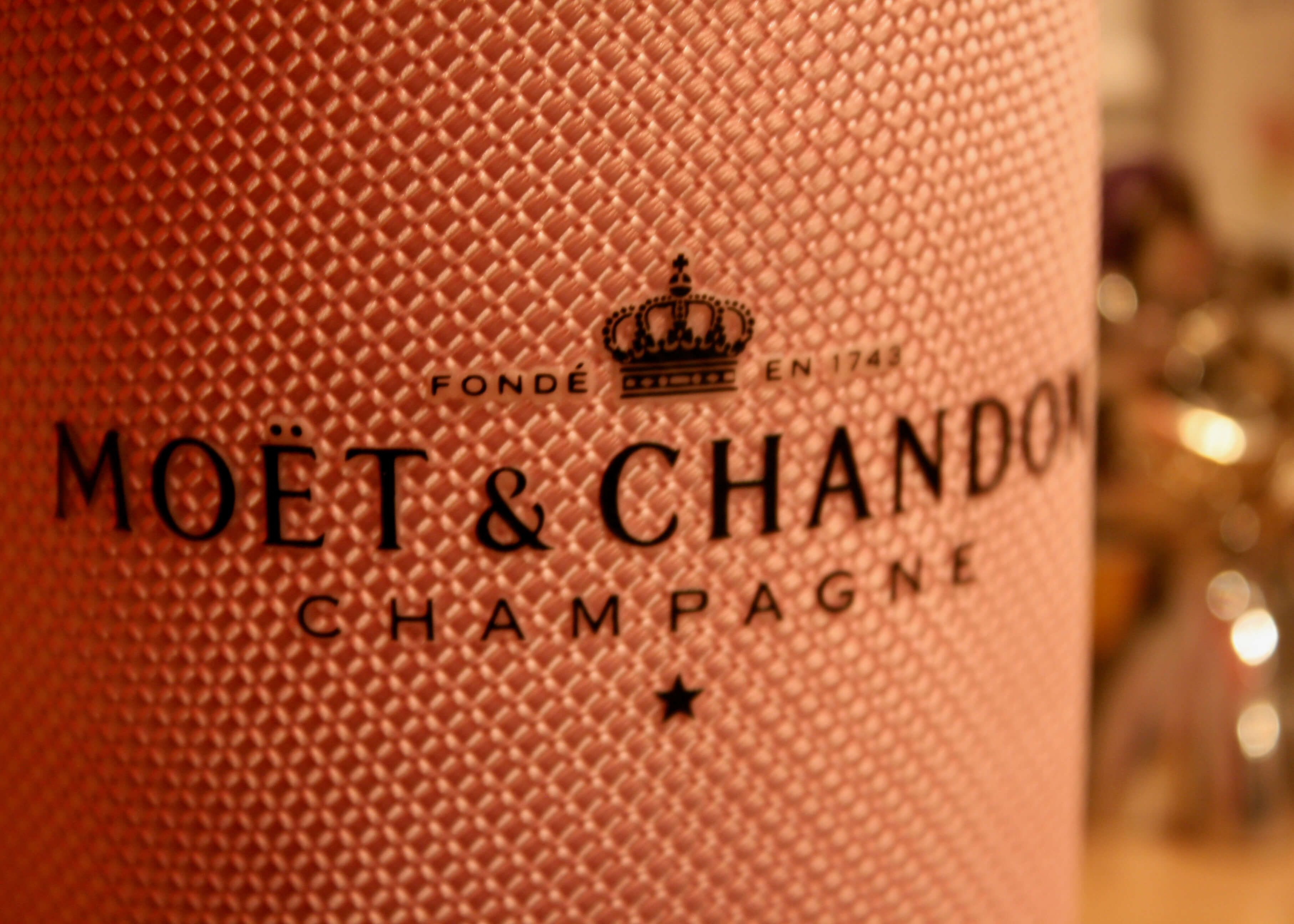 Nærbillede af en tekstureret pink Moët Posters-etiket, der er ideel til brug som champagneplakat eller elegant vægdekoration, og som viser Posters-mærket, et kronelogo og fed CHAMPAGNE-bogstaver.