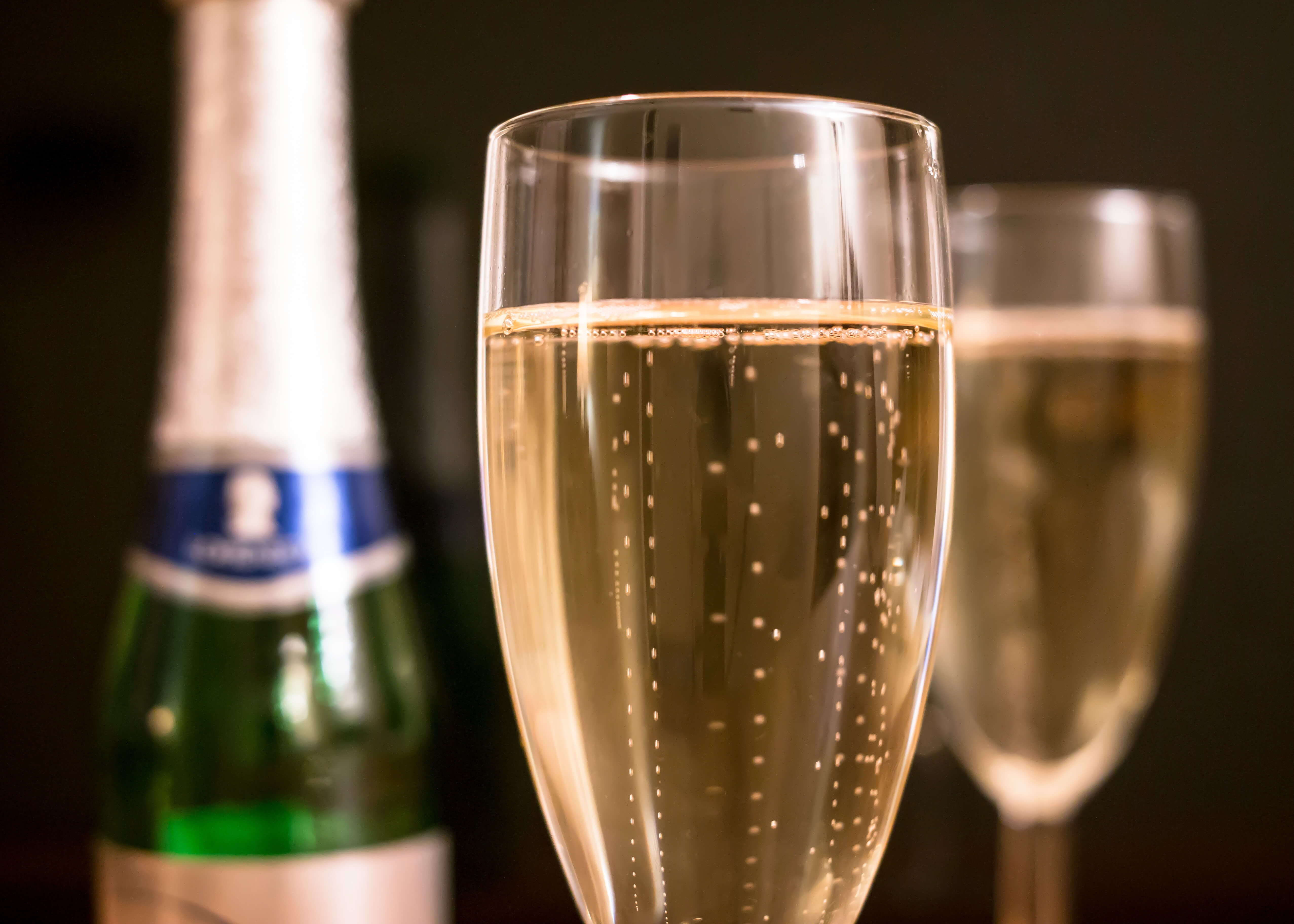 Nærbillede af mousserende champagne i et glas, bobler der stiger op, med et andet glas og en flaske bagved-Posters' "Skål og godt nytår" er det perfekte festlige plakat til enhver fejring eller festlig lejlighed.