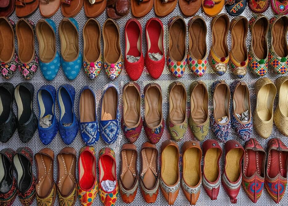 Skomarkedets mangfoldighed by Posters viser en række farverige traditionelle jutti-sko arrangeret i pæne rækker, der fremhæver levende mønstre og iøjnefaldende design som en livlig plakat.