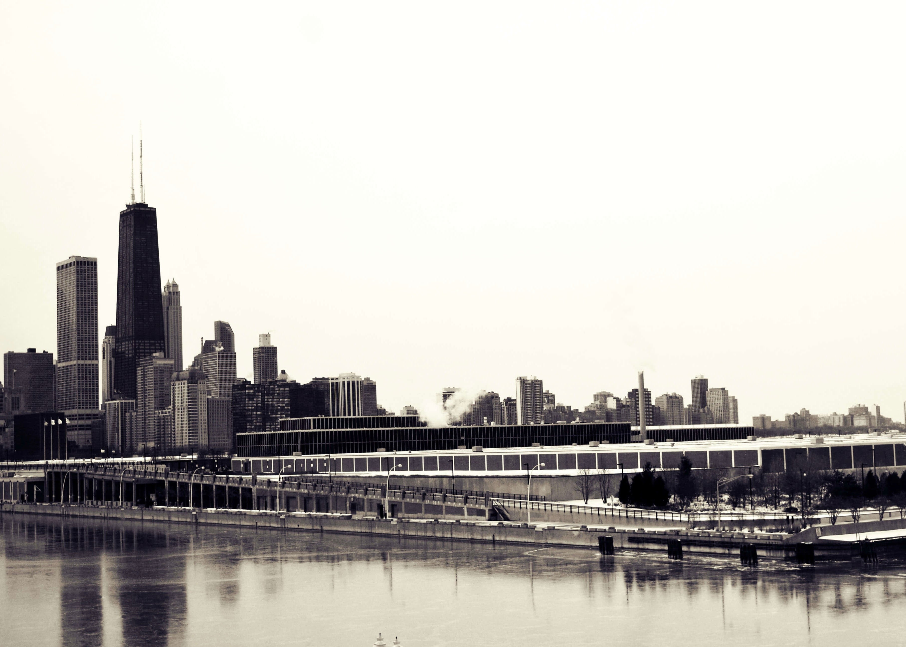 Posters' "Skyline i sorthvid" viser en sort-hvid byskyline med høje bygninger, et fremtrædende tårn og et kongrescenter ved havnefronten, der spejler sig i roligt vand.