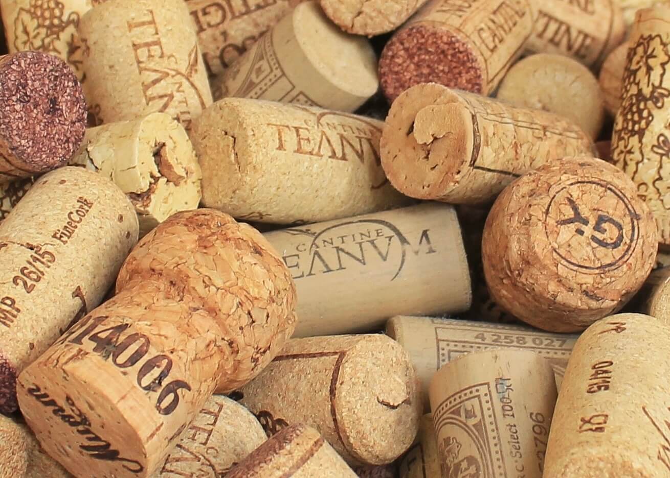 Et nærbillede af Vinpropper by Posters viser en bunke forskellige vinpropper med forskellige teksturer, farver og branding - nogle viser forskellige vingårdsnavne og logoer - og indfanger essensen af vinkultur- og vinflasketraditioner.